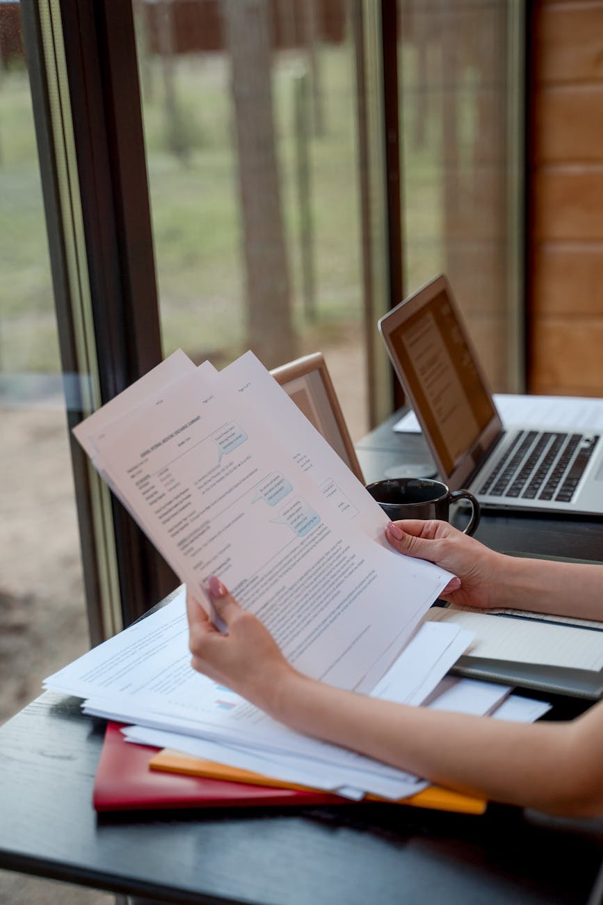 Business professional reviewing candidate resume documents at desk with laptop